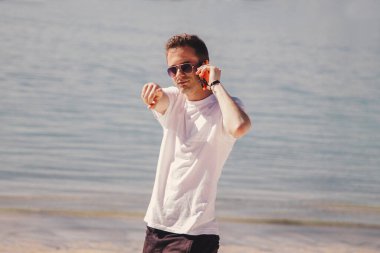 Genç adam kumsalda yürüyor cep telefonuyla konuşuyor ve parmağıyla işaret ediyor.