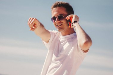 Genç adam kumsalda yürüyor cep telefonuyla konuşuyor ve parmağıyla işaret ediyor.