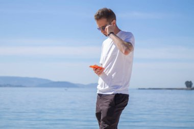 Gülümseyen genç adam rahat ve plajda cep telefonu kullanarak eğleniyor.