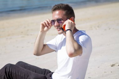 Gülümseyen genç adam rahatlamış ve sahilde eğleniyor.