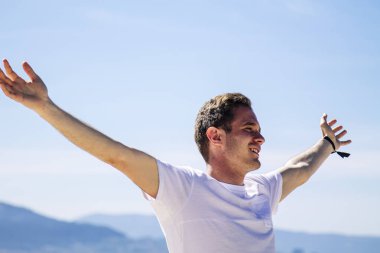 Gülümseyen genç adam rahatlamış ve sahilde eğleniyor.