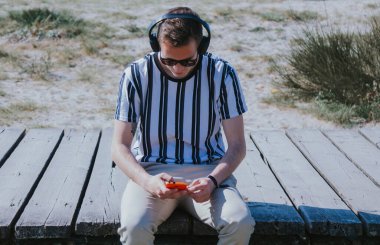 Genç adam cep telefonu ve kulaklıkla oturmuş müzik dinliyor.
