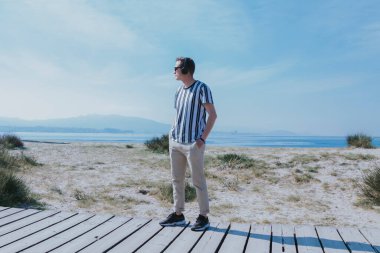 Genç adam plajda kulaklıkla yürüyor ve müzik dinliyor.