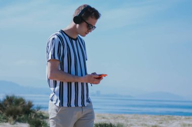 Cep telefonu ve kulaklıkla yürüyen genç adam müzik dinliyor.