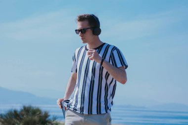 Cep telefonu ve kulaklıkla yürüyen genç adam müzik dinliyor.