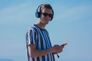 Cep telefonu ve kulaklıkla yürüyen genç adam müzik dinliyor.