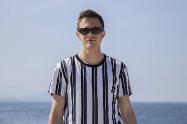 Sahilde güneş gözlüklü gülümseyen genç adamın portresi.