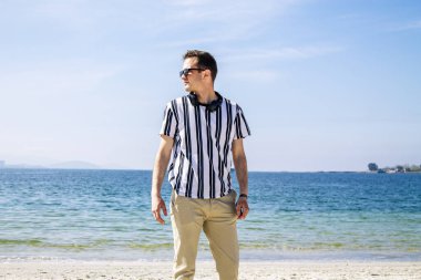 Genç adam plajda kulaklıklarıyla dinleniyor.