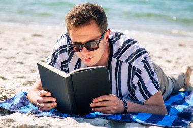 Adam plajda havlusuna uzanmış kitap okuyor.