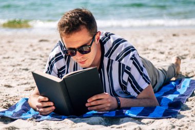 Adam plajda havlusuna uzanmış kitap okuyor.