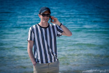 Sahilde cep telefonuyla yürüyen bir adam.