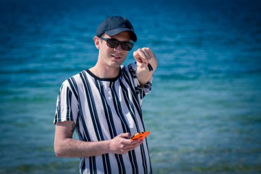 Sahilde cep telefonuyla yürüyen ve parmakla işaret eden adam.