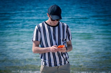 Sahilde cep telefonuyla yürüyen bir adam.