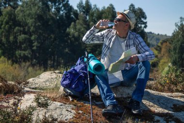 Dağcı içmek için mola veriyor ve haritaya bakıyor.