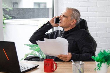 Modern ofiste iş belgeleri ve cep telefonu olan bir işadamı.