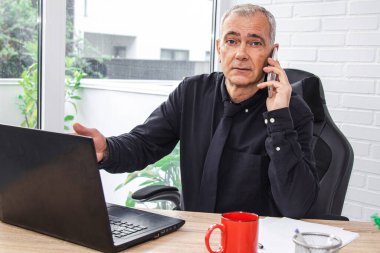 Ofiste bilgisayarla çalışan ve telefonla konuşan bir iş adamı.