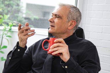 Ofisteki işadamı kahve içiyor ve cep telefonuyla konuşuyor.