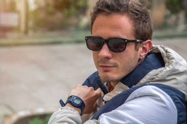 Genç adam merdivenlerde oturmuş saatine bakıyor.