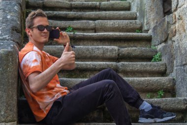 Genç adam cep telefonu kullanıyor ve tamam işareti yapıyor.