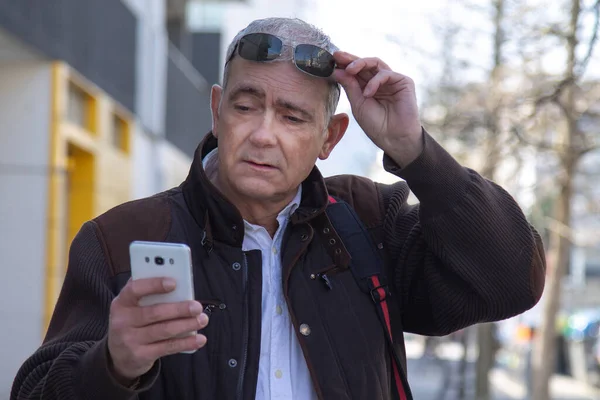 Şık, olgun bir adam sırt çantası ya da çantasıyla şehir kaldırımında yürüyor ve cep telefonunu kullanıyor.