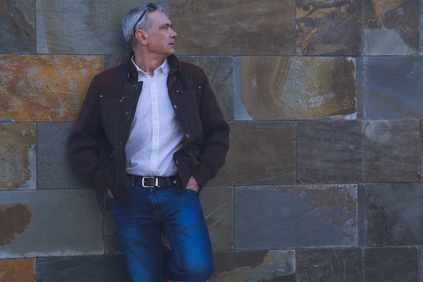 Duvarda kot pantolon ve ceket giyen yetişkin bir adam.