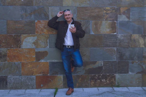 Güneş gözlüklü gülümseyen adam duvar arkası cep telefonu kullanıyor.