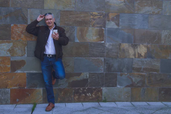 Güneş gözlüklü gülümseyen adam duvar arkası cep telefonu kullanıyor.