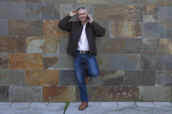 Güneş gözlüklü gülümseyen adam duvar arkası cep telefonu kullanıyor.