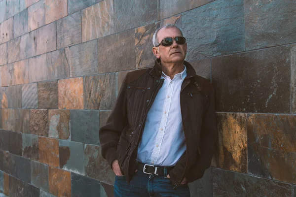 Duvarda kot pantolon ve ceket giyen yetişkin bir adam.