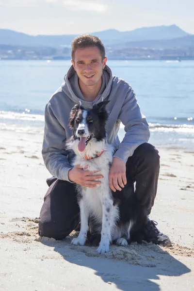 Plajda köpekle rahatlamış genç adamın portresi.