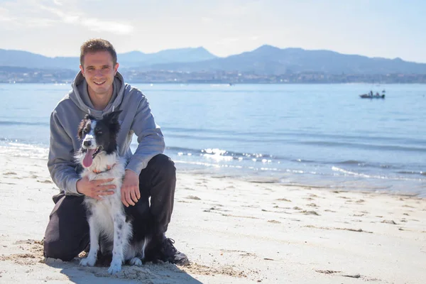 Plajda köpekle rahatlamış genç adamın portresi.