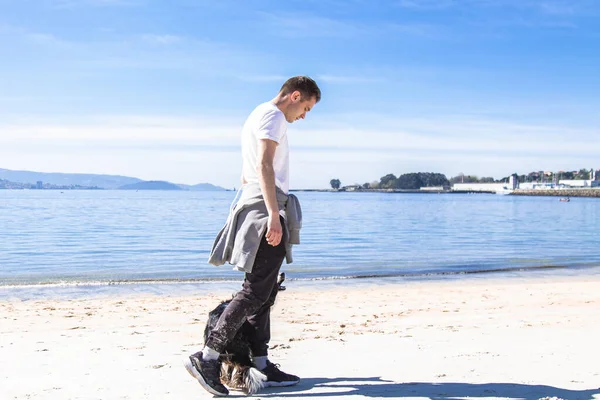 Rahat genç adam sahilde köpekle oynuyor.