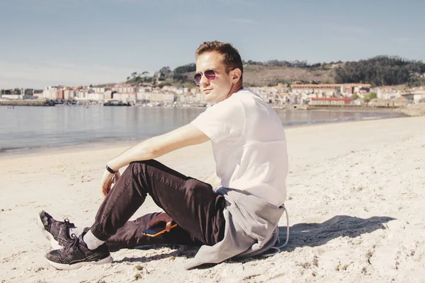 Gülümseyen genç adam rahatlamış ve sahilde eğleniyor.