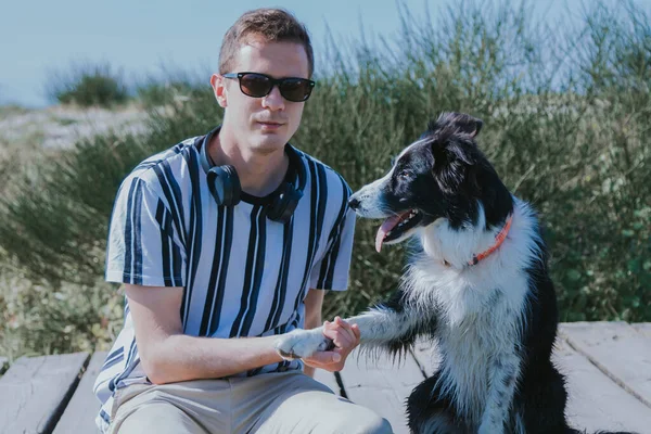 Kulaklıklı bir adam köpeğiyle sahildeki köprüde oturuyor.