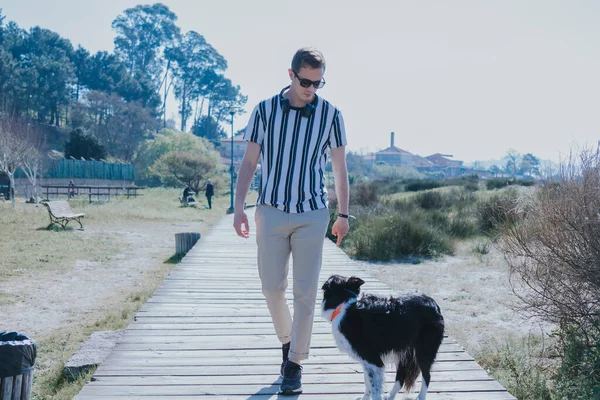 Kulaklıklı bir adam köpeğiyle sahil yolunda yürüyor.