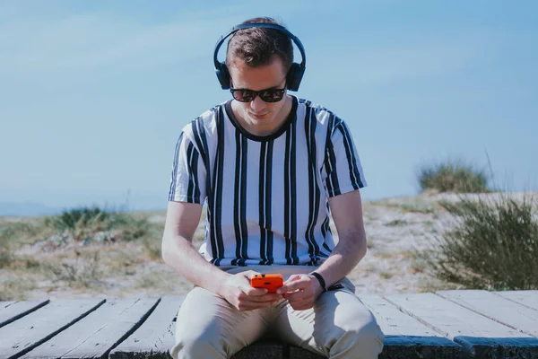 Genç adam cep telefonu ve kulaklıkla oturmuş müzik dinliyor.