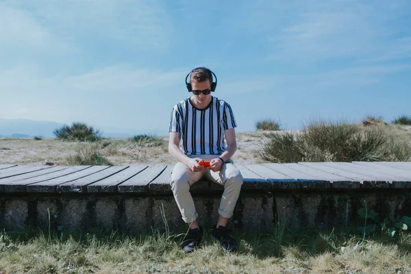 Genç adam cep telefonu ve kulaklıkla oturmuş müzik dinliyor.