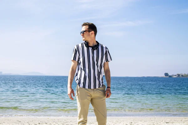 Genç adam plajda kulaklıklarıyla dinleniyor.