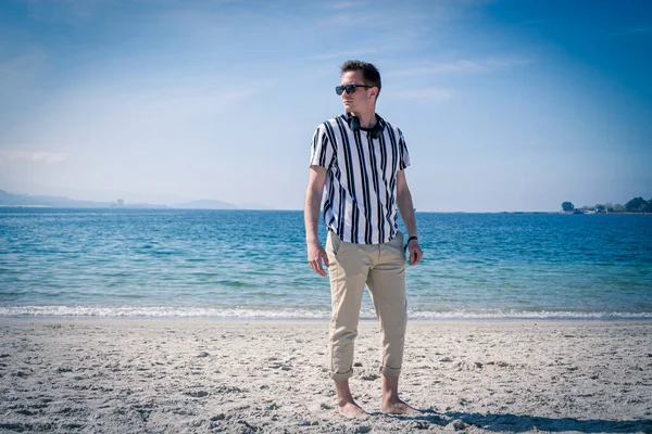 Genç adam plajda kulaklıklarıyla dinleniyor.