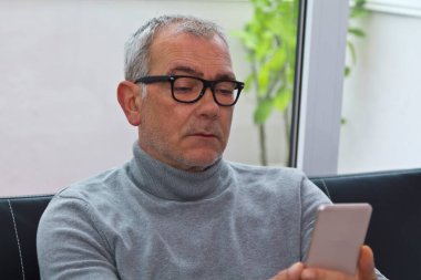 Olgun bir adam evdeki kanepede telefonu kullanıyor.