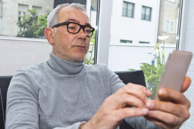 Olgun bir adam evdeki kanepede telefonu kullanıyor.