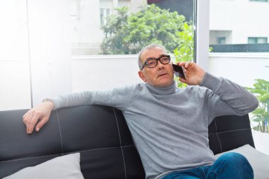 Olgun bir adam evdeki kanepede telefonu kullanıyor.