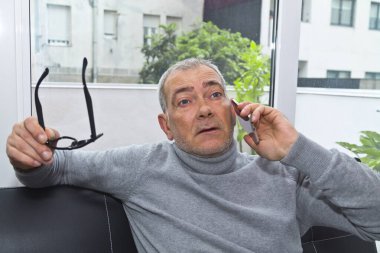 Olgun bir adam evdeki kanepede telefonu kullanıyor.