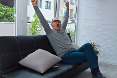 Kollarını kaldırmış, koltukta dinlenen olgun bir adam.