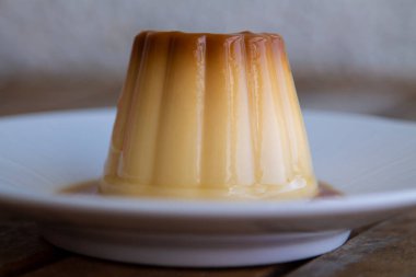 white plate with flan on wooden background, close up view