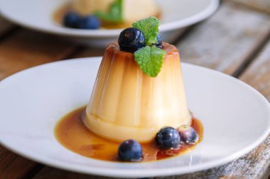 delicious flan with blueberries on white plate on wood