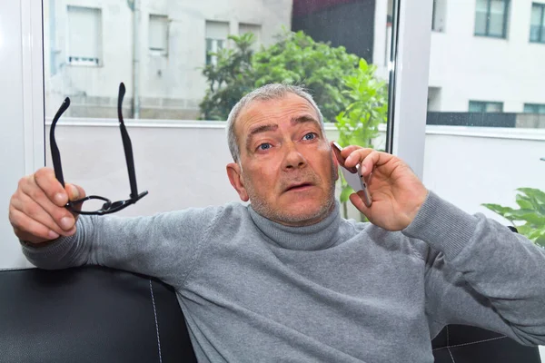 Olgun bir adam evdeki kanepede telefonu kullanıyor.