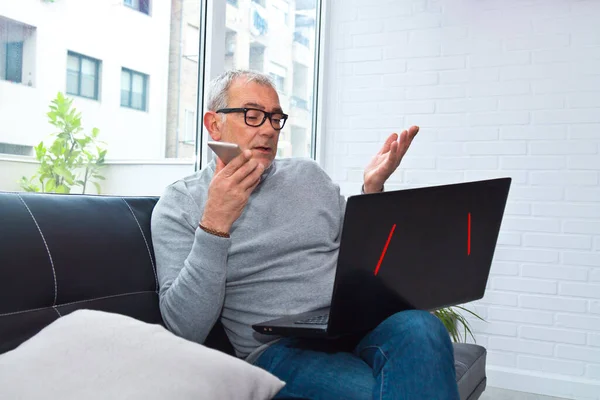 Érett Férfi Használ Laptop Miközben Beszél Telefonon Otthon Vagy Munkahelyen — Stock Fotó