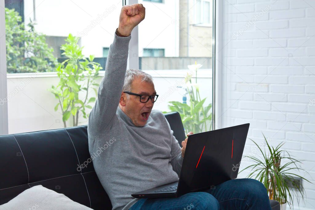 man raising arms in success or victorious sign in front of laptop