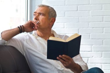 relaxed man reading a book on the armchair and looking out the window
